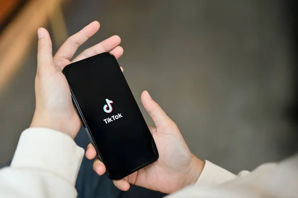 stock image Chiang Mai, Thailand - July 17 2023: An Asian woman using TikTok application on her iPhone14 while relaxing in a coffee shop. TikTok logo on iPhone14 screen in a woman's hands