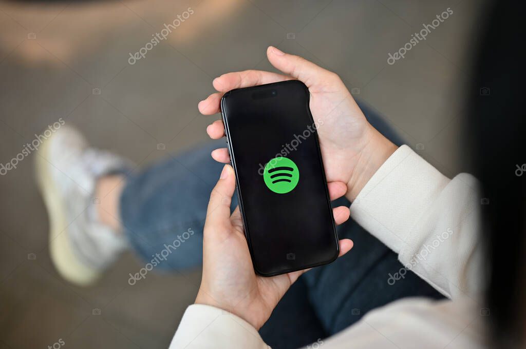 Chiang Mai, Thailand - July 17 2023: A woman holding an iPhone14 with a Spotify logo on screen over blurred background. close-up image