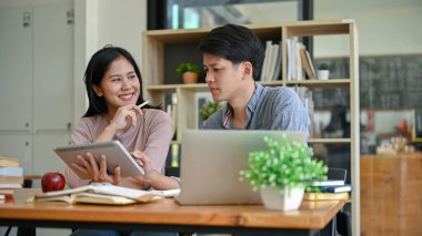 Çekici genç bir Asyalı kız üniversite öğrencisi kampüs kütüphanesinde erkek arkadaşıyla bir proje üzerinde çalışıyor..