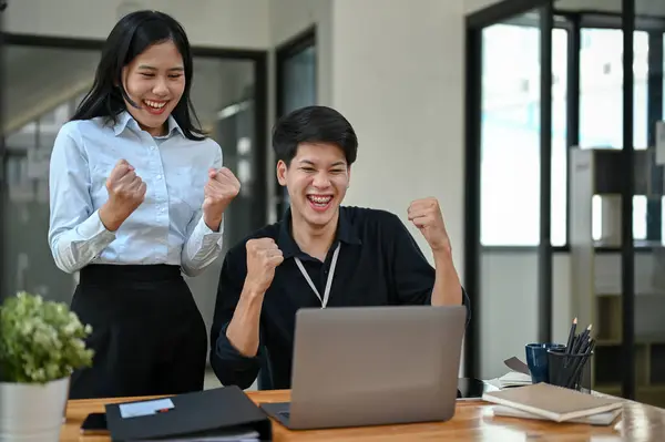 stock image Two cheerful and overjoyed Asian office workers are celebrating their project success together in the office. victory, winning, goal achieved