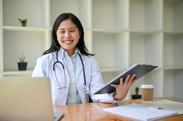 在她的书桌前 一个专业而快乐的年轻亚洲女医生在她的笔记本电脑上工作和阅读医疗案例的肖像 — 图库照片