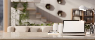 Arka plan olarak bulanık modern oturma odasına karşı dizüstü bilgisayar, kırtasiye malzemesi, masa üstü lambası ve dekoru olan modern bir çalışma alanı. 3d görüntüleme, 3d illüstrasyon