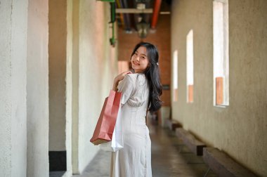 Çekici ve çekici bir Asyalı kadın turistin portresi alışveriş çantalarını taşıyor, binanın içinde yürüyor, hafta sonunun tadını çıkarıyor. Kentsel yaşam tarzı konsepti