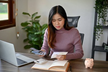 Genç Asyalı kadın vergilerini ve aylık faturalarını hesaplıyor. Masasındaki hesap makinesini kullanarak bütçesini biriktirmeye çalışıyor.