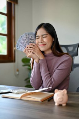 Kişisel yatırım konsepti. Genç gülümseyen Asyalı kadın Piggy Bank 'ı kullanarak para biriktiriyor.. 