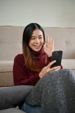 Güzel mutlu bir Asyalı kadının portresi rahat bir süveter videosuyla arkadaşlarıyla birlikte kış tatilinde evde dinlenirken arıyor..