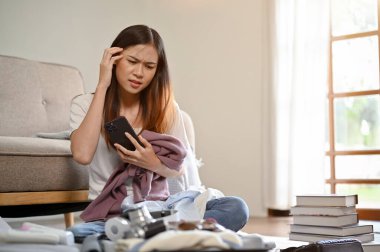 Kafası karışık ve kuşkulu genç bir Asyalı kadın yaz tatili için bavulunu oturma odasında topluyor. tatil, yolculuk, yolculuk