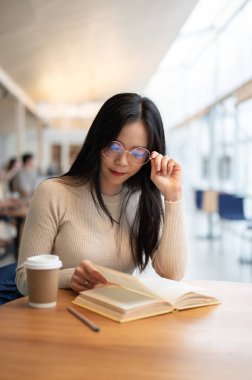 Gözlüklü güzel, zeki, Asyalı genç bir üniversite öğrencisinin portresi bir kafede birlikte çalışırken kitap okumaya odaklanıyor..