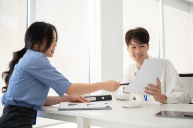 İki profesyonel Asyalı genç ofis çalışanı iş görüşmeleri yapıyor, bir proje planlıyor ve ofiste raporları birlikte inceliyorlar..