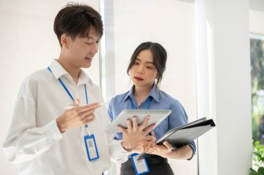 İki profesyonel ve odaklanmış Asyalı ofis çalışanı şirket koridorunda birlikte dururken iş hakkında konuşuyor ve tartışıyorlar..