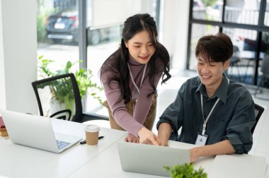 Profesyonel ve arkadaş canlısı Asyalı bir bayan pazarlama asistanı, bir dizüstü bilgisayardan ayrıntıları okuyor ve erkek meslektaşına bir pazarlama kampanyasında yardım ediyor..