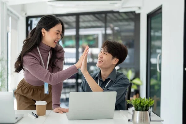 Two cheerful and happy young Asian business people give high fives to each other to celebrate their successful project together. teamwork, cheer-up, team building