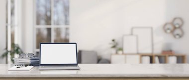 Modern bir çalışma alanı, dizüstü bilgisayar beyaz ekran modeli, kitaplar, gözlükler, ve masa üstü, bulanık modern beyaz oturma odası arka planında kopya alanı. 3d görüntüleme, 3d illüstrasyon