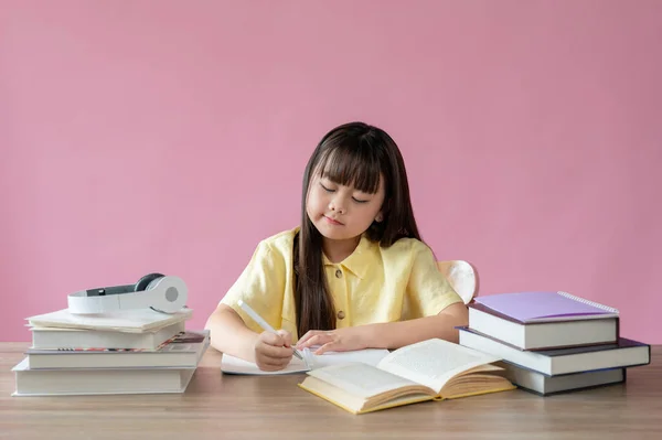 一位可爱的年轻亚洲女孩正把注意力集中在自己的功课上 面对着一个孤立的粉色背景 小学生概念 — 图库照片