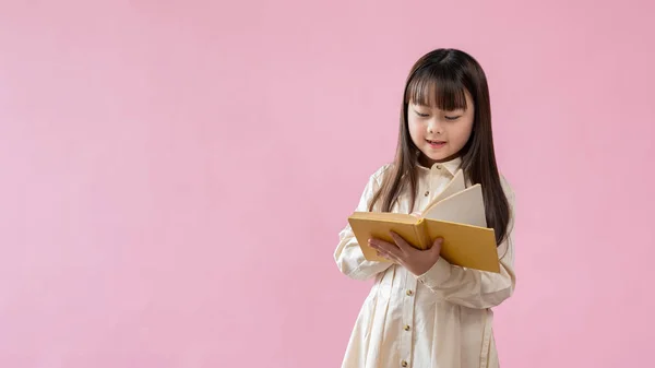 一个可爱而快乐的年轻亚洲女孩站在一个孤立的粉色工作室的背景下 正在看书或童话故事 小学生 — 图库照片