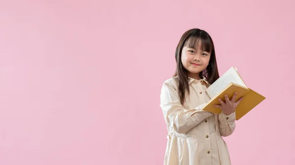一个聪明可爱的年轻亚洲女孩站在一个孤立的粉色工作室背景下 手里拿着一本书 小学生 休闲和业余爱好 — 图库照片