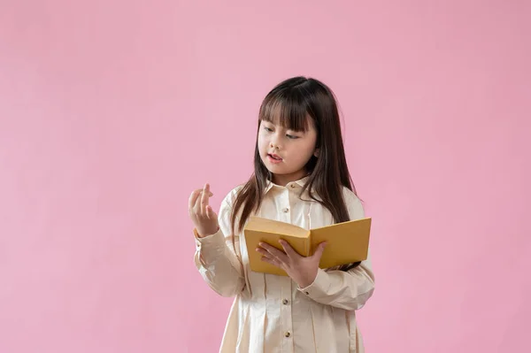 一位可爱的年轻亚洲女孩一边拿着一本书 一边专注于计数数字 站在一个孤立的粉色工作室的背景下 小学学生 家庭学校 — 图库照片