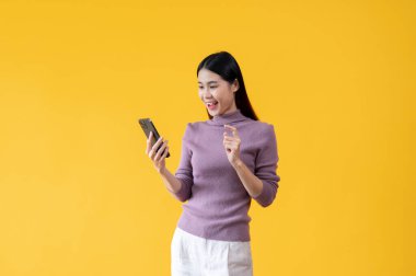 Güzel bir Asyalı kadın akıllı telefonunu kullanıyor, sohbet ediyor, SMS veya e-posta gönderiyor, sosyal medyada kayıyor, blogunu güncelliyor, mobil uygulamalar kullanıyor ve çevrimiçi alışverişin tadını çıkarıyor. izole edilmiş sarı arkaplan
