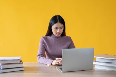 Güzel ve kendinden emin Asyalı bir iş kadını laptopuyla işine odaklanıyor, masasındaki görevini yönetiyor. izole edilmiş sarı arkaplan