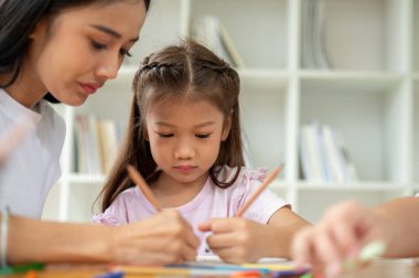 Sevimli bir Asyalı ilkokul öğrencisi sınıfta bir öğretmenle ders çalışmaya, yazmaya ya da kağıda bir şeyler çizmeye odaklanıyor. Çocuk eğitimi konsepti