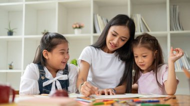 Nazik bir Asyalı kadın bebek bakıcısı veya özel öğretmen, genç çocuklara resim ve boyama yapmaktan zevk alarak sanat öğretiyor. Çocuklar, anaokulu çocukları, ilkokul öğrencileri.