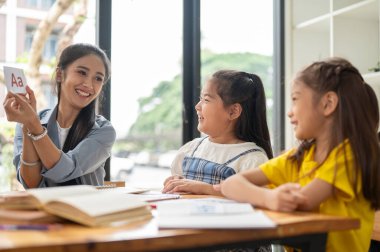 Sevimli genç bir Asyalı kız evde arkadaşıyla birlikte özel bir öğretmenle İngilizce çalışmaktan zevk alıyor. Anaokulu, anaokulu, ilkokul öğrencisi, ev okulu.