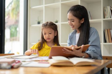 Şefkatli bir anne evde küçük kızına İngilizce öğretiyor ve yardım ediyor. Mutlu aile, bebek bakıcılığı, ev okulu, özel öğretmen.