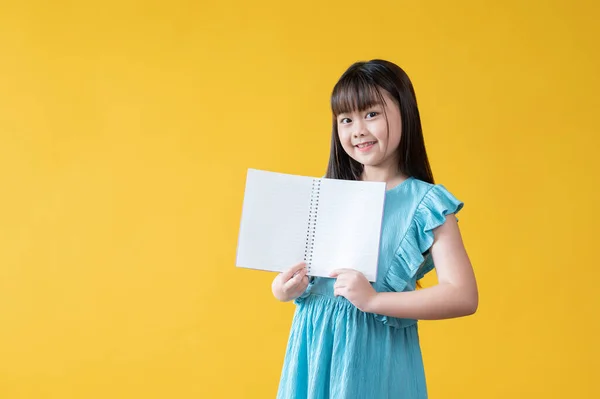 一个身穿蓝色衣服的漂亮的亚洲小女孩 手里拿着一本翻开的书 上面空空如也 面带微笑地看着相机 孤立的黄色背景 Kids Child Students Education Learning — 图库照片