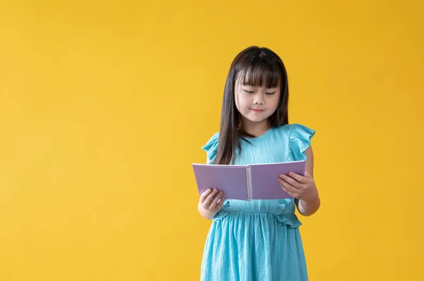 一个身穿漂亮蓝色衣服的快乐可爱的年轻亚洲女孩站在孤立的黄色背景下看书或她最喜欢的童话故事 爱好和知识 — 图库照片