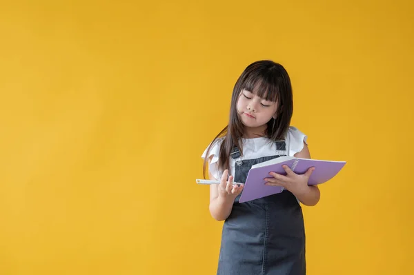 一个可爱的亚洲小女孩正站在一个孤立的黄色背景下 专注于计数数字和做作业 小学生 — 图库照片