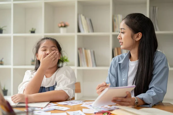 A beautiful and kind Asian female teacher or private tutor is talking and convincing a sleepy lazy girl to study and pay attention to a lesson.