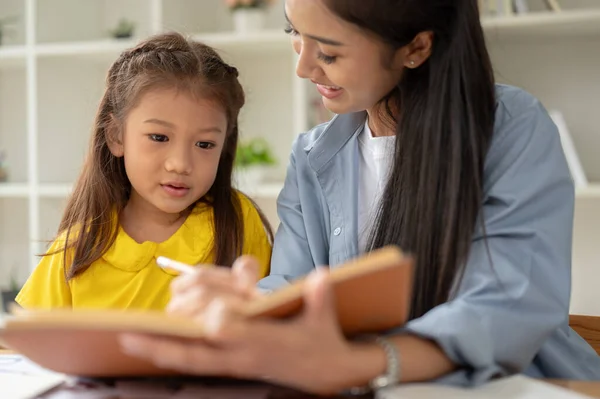 An adorable little Asian girl is focusing on studying with a kind private teacher at home. babysitting, sisters, mother and daughter, preschool kid