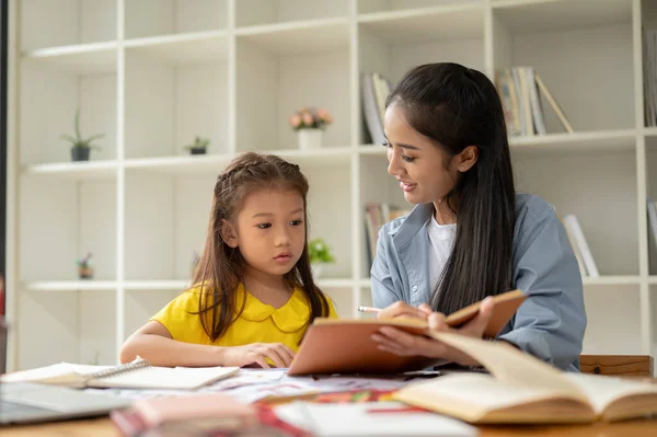 A pretty Asian preschool girl is studying English alphabet with a kind and caring female teacher. A caring mom helping and teaching English a her little daughter at home.