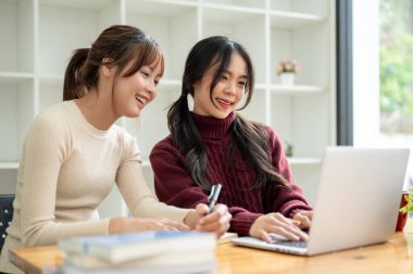 İki güzel ve mutlu Asyalı kız üniversite öğrencisi ödev yapıyor ve bir kafede ortak proje üzerinde çalışıyorlar..