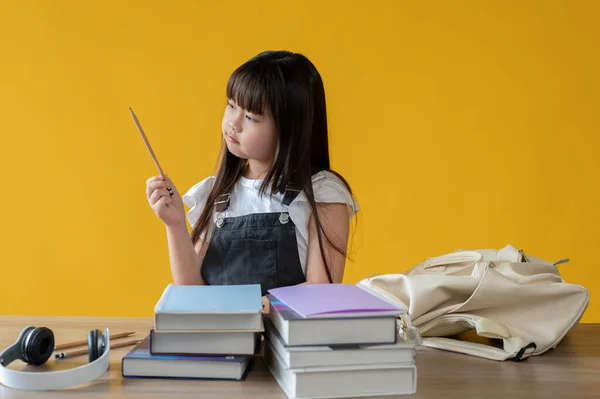 一位可爱的年轻亚洲女孩正在为她上学的日子准备文具 她的桌旁有一个孤立的黄色背景 女学生概念 — 图库照片