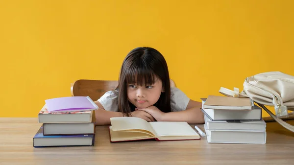 一个可爱的年轻亚洲女孩 她坐在自己的学习桌上 脸上无精打采 不想学习或做作业 因为她太懒而不能看书 在孤立的黄色背景上 — 图库照片