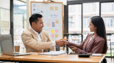 Profesyonel bir Asyalı işadamı ofisteki bir masada bayan bir meslektaşıyla tokalaşıyor. Tebrikler, takım çalışması, hoş geldiniz, anlaşma