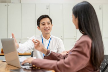 Profesyonel bir Asyalı işadamı, ofisteki bir bayan meslektaşıyla yeni bir proje için çalışma ve planlar hakkında konuşuyor..