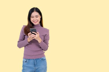 Güzel bir Asyalı kadın akıllı telefonunu kullanıyor, sohbet ediyor, SMS veya e-posta gönderiyor, sosyal medyada kayıyor, blogunu güncelliyor, mobil uygulamalar kullanıyor ve çevrimiçi alışverişin tadını çıkarıyor. izole edilmiş sarı arkaplan