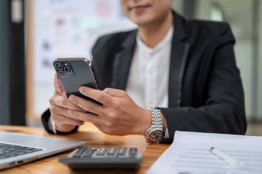 Ofisteki masasında akıllı telefonunu kullanan mutlu ve profesyonel bir Asyalı iş adamının yakın plan görüntüsü. metin, sohbet, SMS, e-posta, uygulamalar