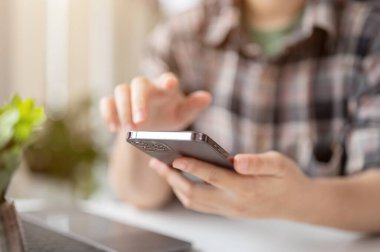 Flanel gömlekli bir kadının masadaki akıllı telefonunu kullanışının yakın plan görüntüsü. İnsanlar ve teknoloji kavramı