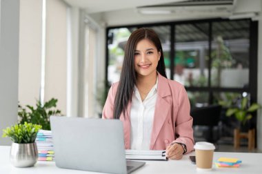 Güzel Asyalı bir iş kadınının portresi ya da pembe takım elbiseli bir kadın yönetici modern bir ofiste masasında oturuyor.. 