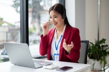 Kendine güvenen ve güzel bir Asyalı kadın müşteri hizmetleri operatörü veya çağrı merkezi temsilcisi telefon ya da video üzerinden bir müşteriye konuşuyor ve tavsiyelerde bulunuyor. 
