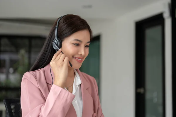 A beautiful Asian female call centre operator with a headset is having a conversation with a customer over the phone in the office. customer service, support team, call center agent
