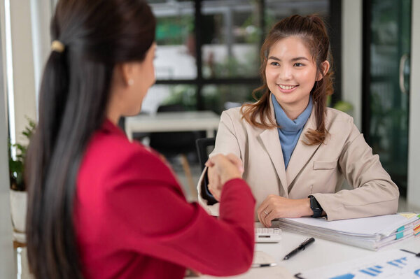A professional Asian female financial analyst or consultant is shaking hands with her client after the financial investment meeting. partnership, dealing, business negotiation, teamwork