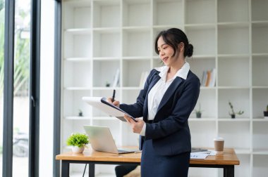 Profesyonel ve çekici Asyalı bir iş kadını ofisinde dururken panoya bir şeyler yazıyor..