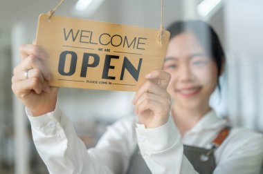 Mutlu ve güzel bir Asyalı bayan restoran çalışanının ya da garsonun yakın plan resmi giriş kapısına açık bir tabela asıyor. Hoşgeldiniz işareti, açık işaret, kullanılabilir