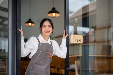 Neşeli, Asyalı genç bir bayan kahve dükkanı sahibi ya da önlüklü bir garson dükkanının girişinde duruyor. restaurant, shop, store, cafe