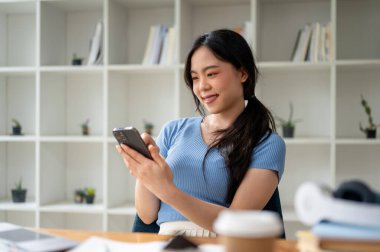 Güzel bir Asyalı kadın masasında akıllı telefonunu kullanıyor arkadaşlarıyla sohbet ediyor, sosyal medyada kayıyor ya da uygulamadan alışveriş yapıyor..