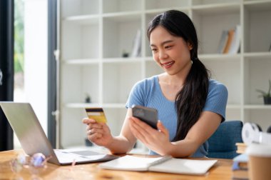 Mutlu genç Asyalı bir kadın evde online alışveriş yapmaktan ve kredi kartıyla ödemekten hoşlanıyor. Nakitsiz ödeme, e-ticaret, online alışveriş, mobil bankacılık 